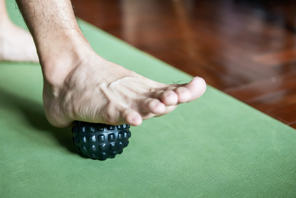 A massage ball is rolled under a foot to relieve plantar fasciitis pain.